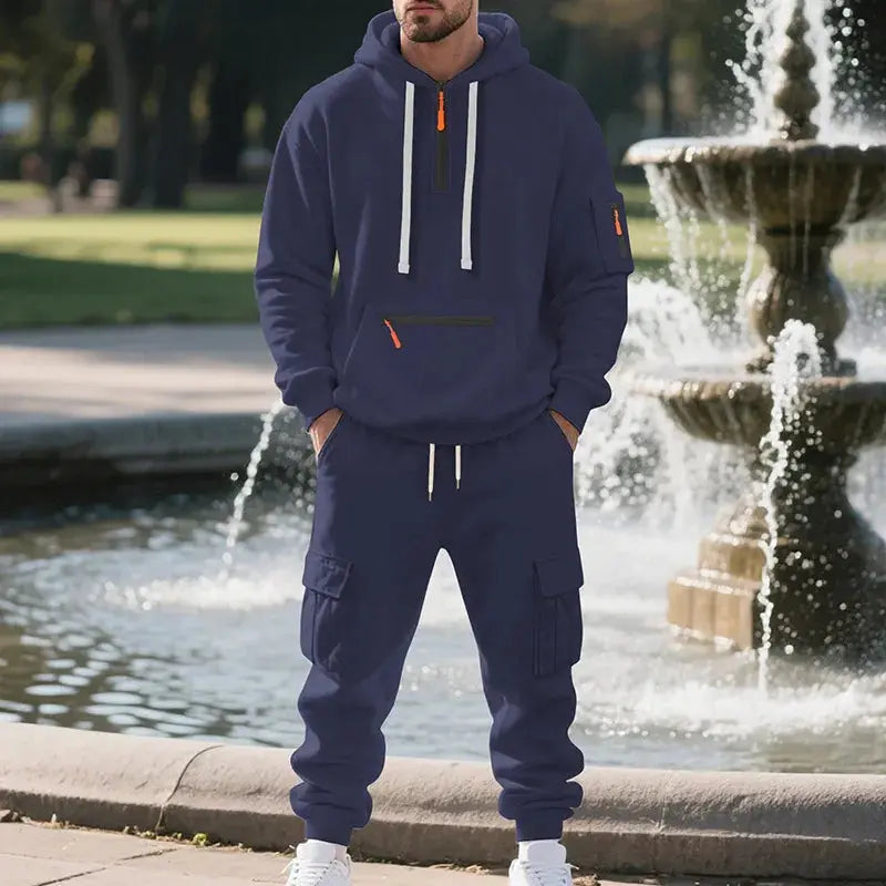 Man wearing a navy blue tracksuit standing in front of a fountain.