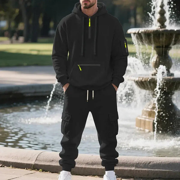Person wearing a black hoodie and pants with neon accents standing in front of a fountain.