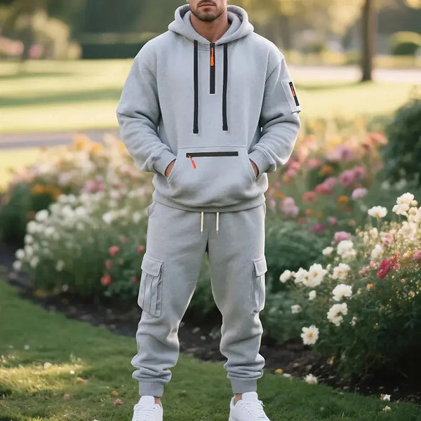 Person wearing a gray tracksuit standing in a garden with flowers and greenery.